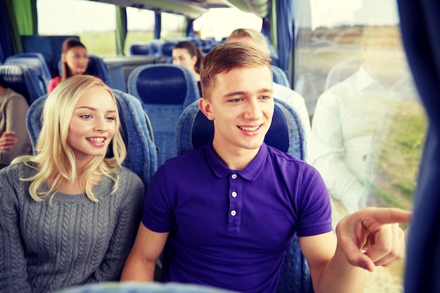 transport, tourism, road trip and people concept - happy teenage couple with group of passengers or tourists in travel bus