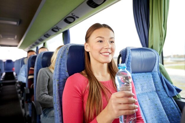 Photo transport, tourism, road trip and people concept - happy young woman with water bottle in travel bus