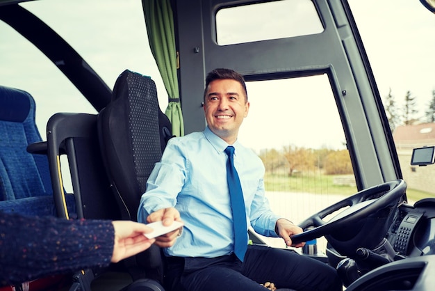 концепция транспорта, туризма, дорожного путешествия и людей - улыбающийся водитель автобуса берет билет или пластиковую карту у пассажира