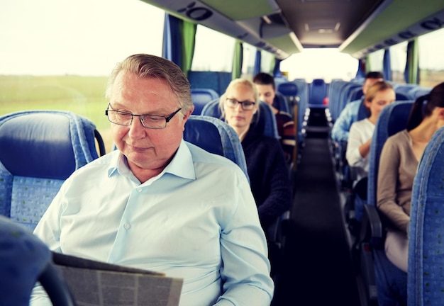 transport, tourism, trip and people concept - senior man reading newspaper in travel bus