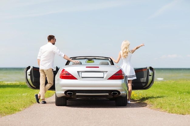 transport, travel, road trip and people concept - happy man and woman near cabriolet car at sea side