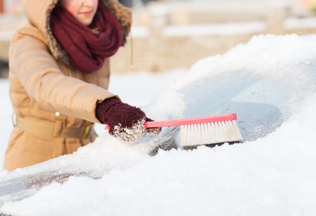 transport-, winter- en voertuigconcept - close-upvrouw die sneeuw van de achterruit van de auto schoonmaakt met borstel