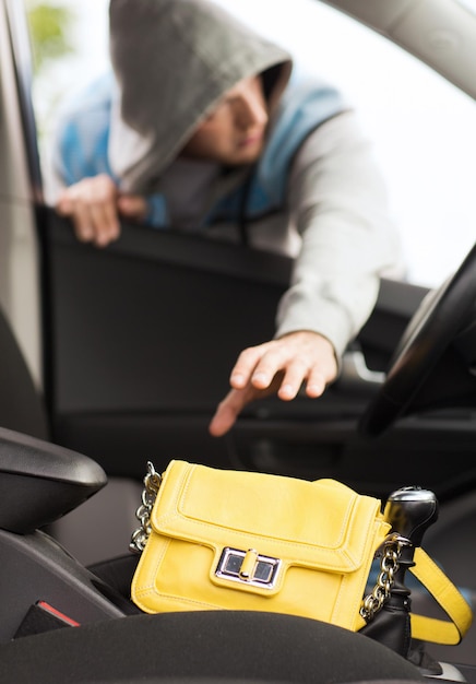 transportation, crime and ownership concept - thief stealing bag from the car