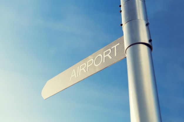 transportation, direction, location, travel and road sign concept - close up of airport signpost over blue sky background