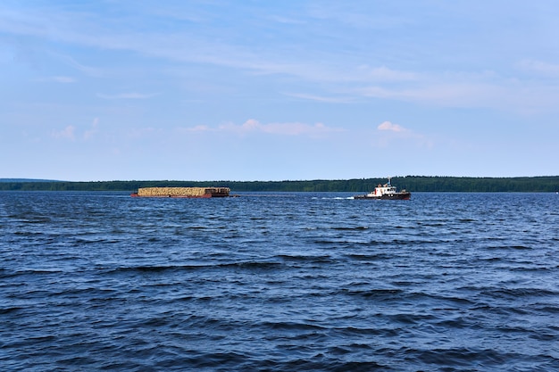 Transportation of timber along the river using a barge towed by a tug