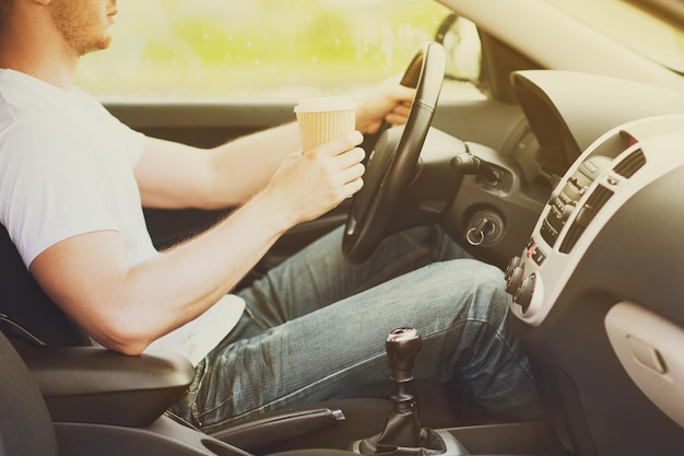 transportation and vehicle concept - man drinking coffee while driving the car