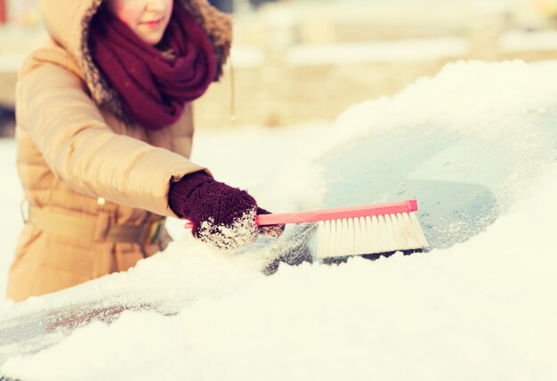 写真 交通機関、冬、車のコンセプト-ブラシで車の後ろの窓から雪を掃除するクローズアップの女性