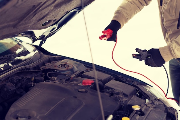 transportation, winter and vehicle concept - closeup of man under bonnet with starter cables