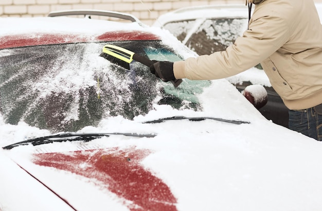 交通機関、冬、車のコンセプト-ブラシで車のフロントガラスから雪を掃除する男のクローズアップ