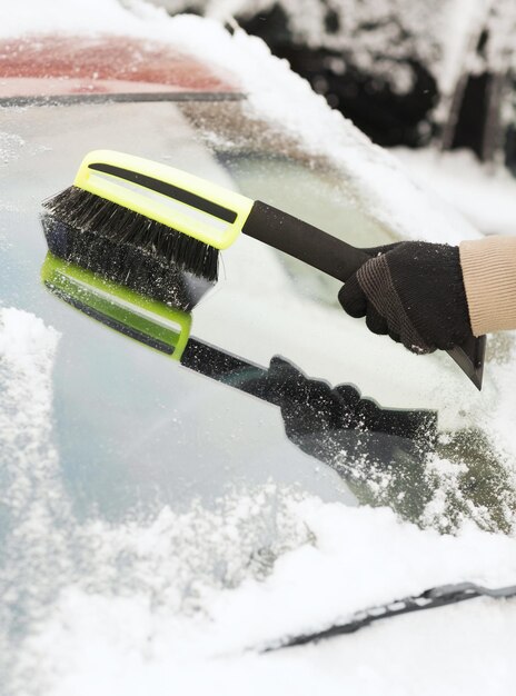 transportation, winter and vehicle concept - closeup of man cleaning snow from car windshield with brush