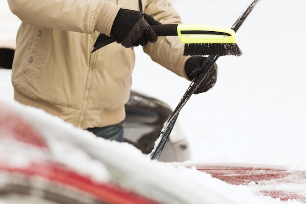 交通機関、冬、車のコンセプト-ブラシで車のフロントガラスから雪を掃除する男のクローズアップ