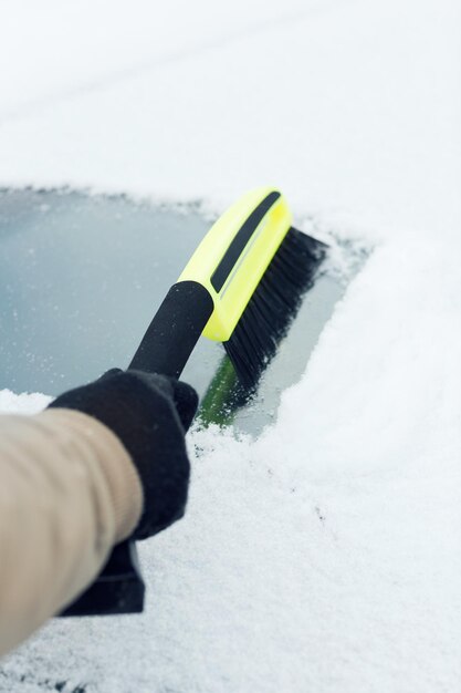 交通機関、冬、車のコンセプト-ブラシで車のフロントガラスから雪を掃除する男のクローズアップ