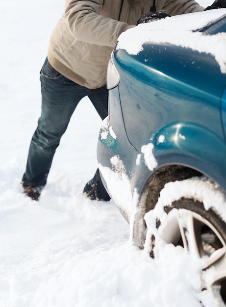 transportation, winter and vehicle concept - closeup of man pushing car stuck in snow