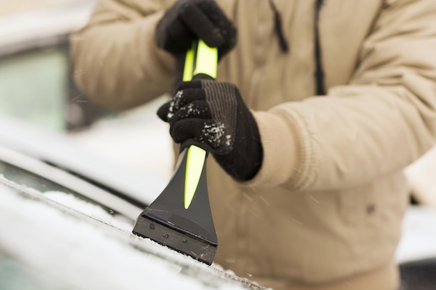 transportation, winter and vehicle concept - closeup of man scraping ice from car windshield with brush