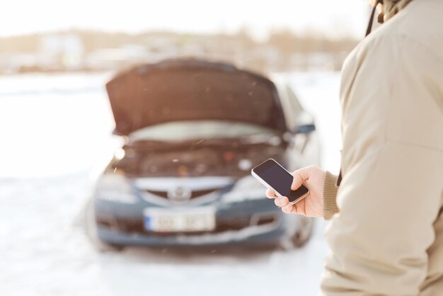 transportation, winter and vehicle concept - closeup of man with broken car and smartphone