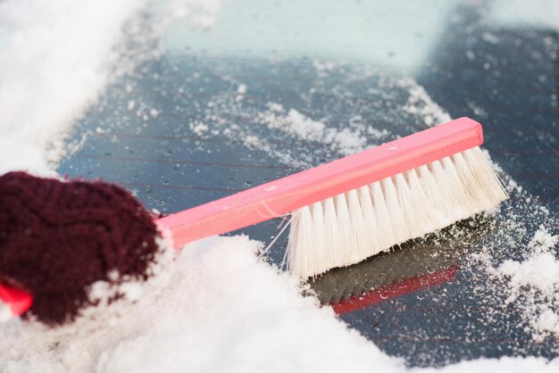 transportation, winter and vehicle concept - closeup woman cleaning snow from car back window with brush