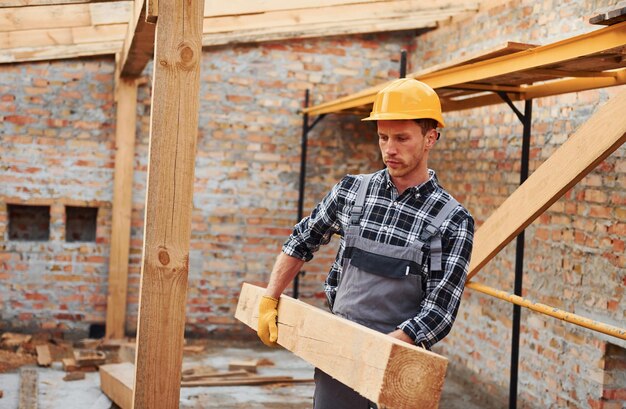 Фото Транспортировка деревянных досок строитель в униформе и защитном снаряжении работает на строительстве