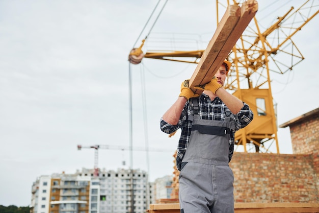 Transporting wooden boards Construction worker in uniform and safety equipment have job on building