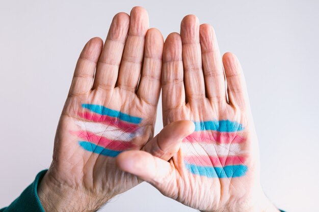 Мужчина-транссексуал поднимает руки с нарисованным на ладонях флагом транссексуала