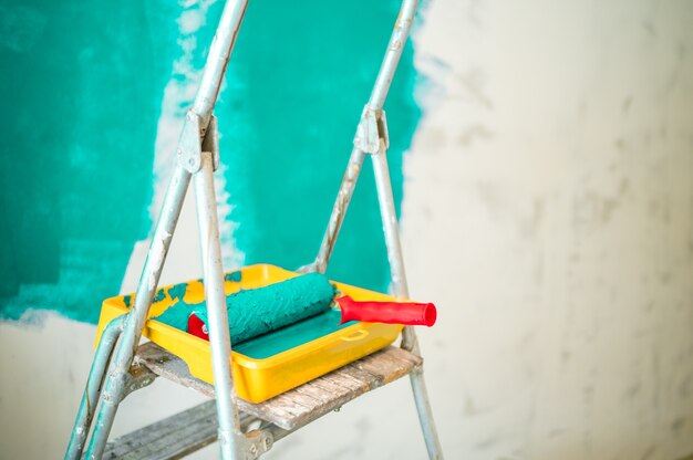 Trapladder, verfbak en roller op de achtergrond van een ongeverfde turquoise muur