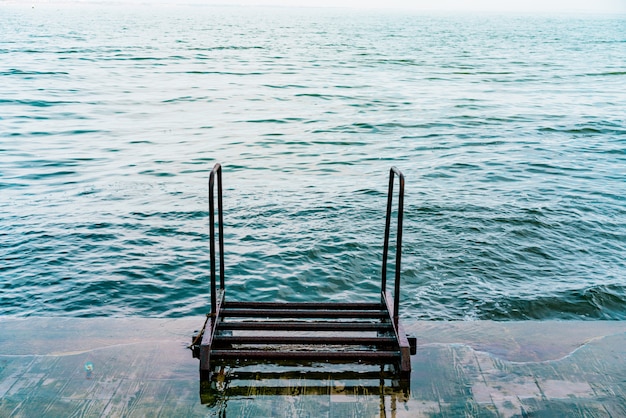 Trapleuning naar beneden naar de blauwe zee. metalen trap. trap ingang naar de golvende zee. dijk. water met golven. zomer. geen mensen op de boulevard. niemand. leeg. winderig. leuningen