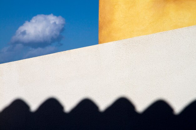 Trapped cloud. two exterior walls of the house, white and yellow, bound a small piece of blue sky where a small cloud flies