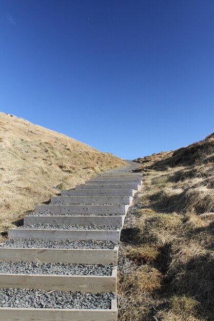 Foto trappen die naar de top van de berg leiden tegen een heldere blauwe hemel.