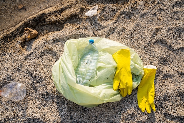 Il sacco della spazzatura e i guanti giacciono sulla sabbia. pulizia e concetto di protezione dell'ambiente.