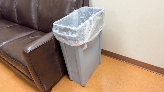 A trash can in a waiting room with a chair in the background.