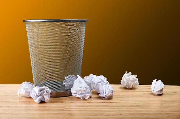 Trash can with paper sheets on wooden table