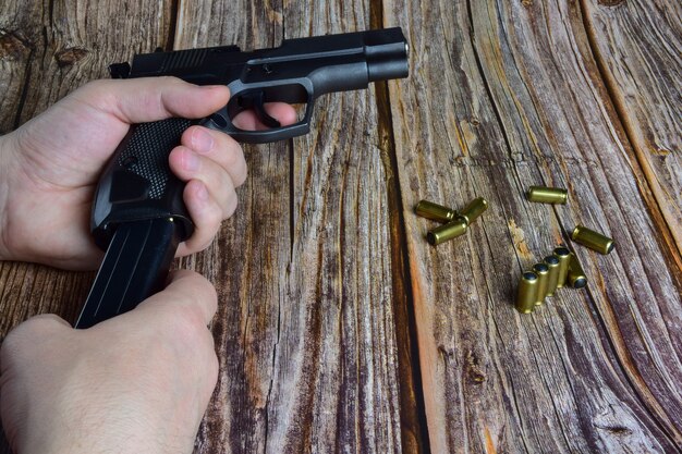 Traumatic cartridges are scattered on a brown wooden background. Hands hold a pistol clip and a pistol