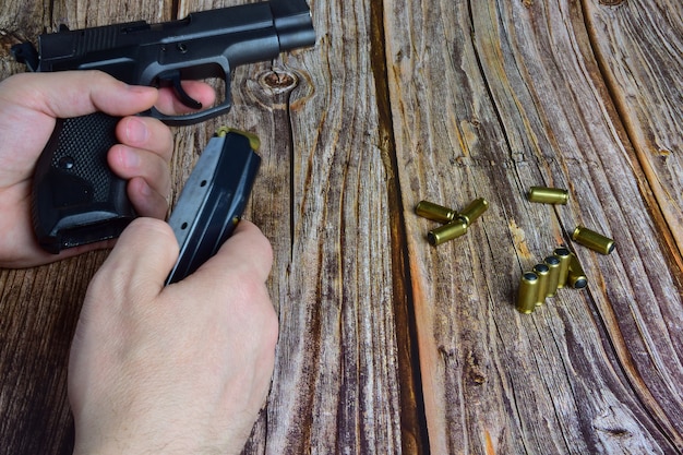 Foto traumatische patronen zijn verspreid over een bruine houten ondergrond. handen houden een pistoolklem en een pistool vast