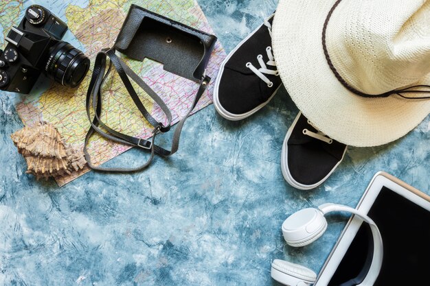 Travel accessories camera, straw hat, card, shoes on a blue background flat top view layout with copy space