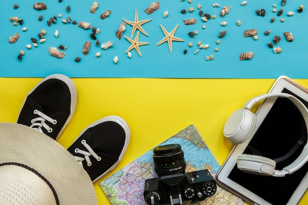 Travel accessories camera, straw hat, card, shoes on a  yellow bluebackground flat top view layout with copy space