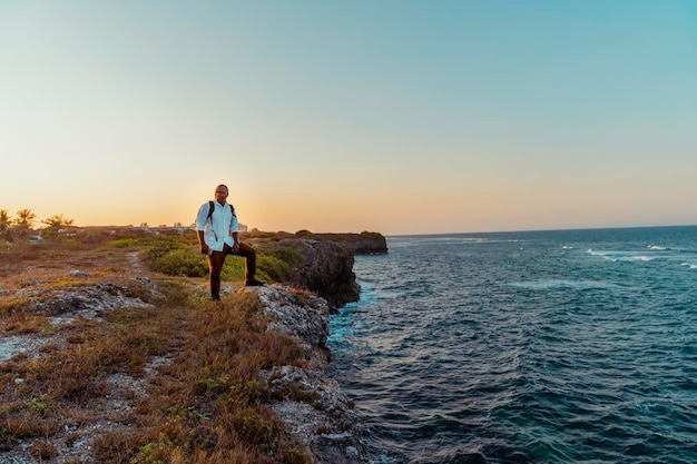 夕日の景色を楽しみながら海の崖の上に立っているアフリカ人旅行