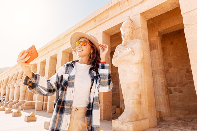 Photo travel blogger girl takes selfie pictures on a smartphone at the famous hatshepsut temple in the ancient city of luxor in egypt tourism attractions and destinations