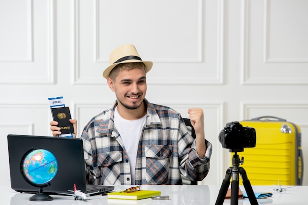 밀짚모자를 쓴 여행 블로거 젊고 잘생긴 남자가 티켓에 만족하는 카메라에 여행 Vlog를 기록합니다.