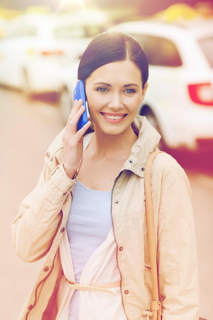 travel, business trip, people and tourism concept - smiling young woman calling and talking on smartphone over taxi station or city street