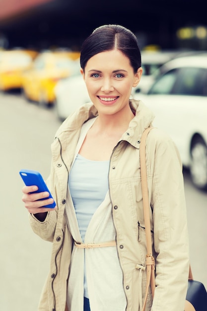 travel, business trip, people and tourism concept - smiling young woman with smartphone over taxi station or city street