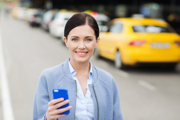 travel, business trip, people and tourism concept - smiling young woman with smartphone over taxi station or city street