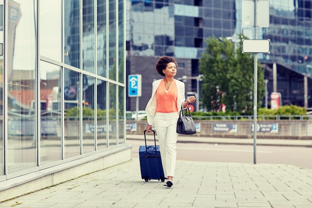 여행, 출장, 사람, 관광 개념 - 여행 가방을 들고 도시 거리를 걷고 있는 젊은 아프리카계 미국인 여성