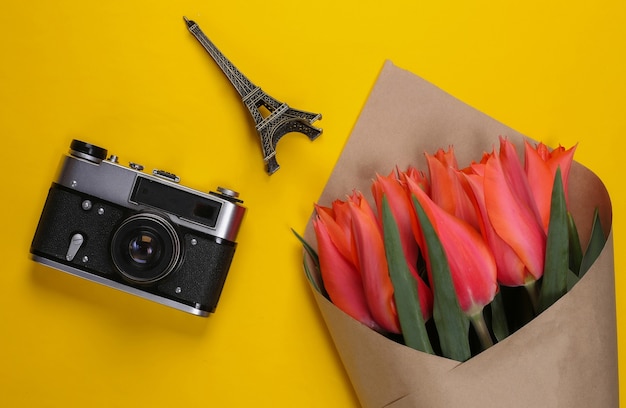 Foto concetto di viaggio. mazzo di tulipani, macchina fotografica, statuetta della torre eiffel su un giallo