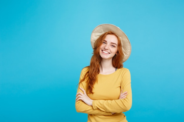 旅行のコンセプトは、トレンディな帽子と笑顔の青いパステルカラーの壁のコピースペースを持つ肖像画の若い美しい魅力的な生姜赤い髪の少女をクローズアップ