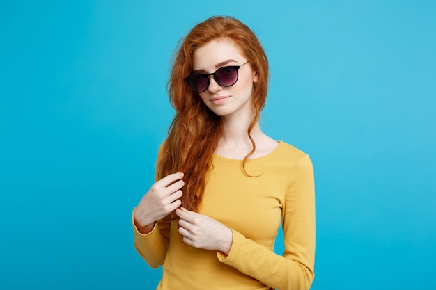Travel concept - Close up Portrait young beautiful attractive ginger red hair girl with trendy sunglass smiling. Blue Pastel Background. Copy space.