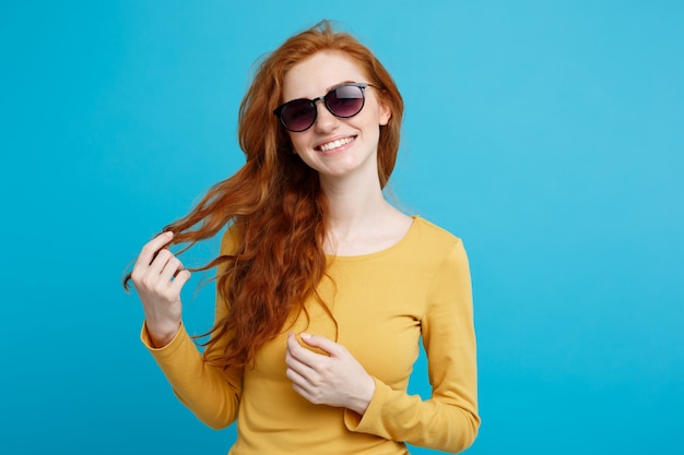 Travel concept - Close up Portrait young beautiful attractive ginger red hair girl with trendy sunglass smiling. Blue Pastel Background. Copy space.