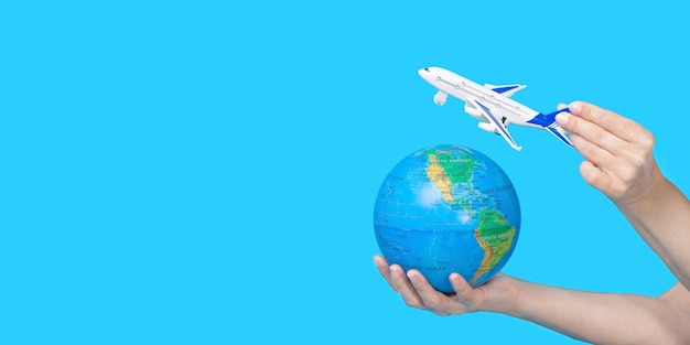 Travel concept. Female hands holding globe and figurine of passenger plane on blue background. The plane is flying to the globe.