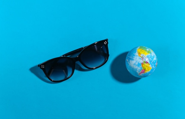 旅行のコンセプト。青い背景のメガネと地球儀。上面図。フラットレイ。ミニマリズム