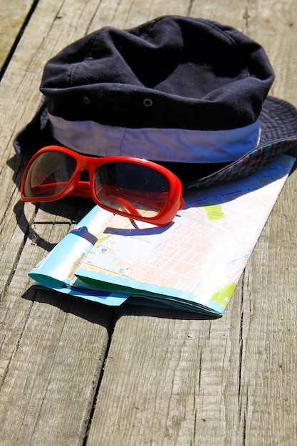 Travel concept. Hat, red sunglasses and map on wooden background