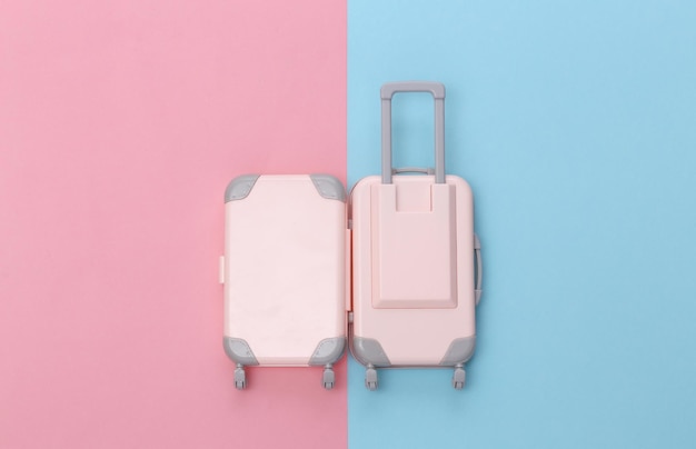 Travel concept. Mini plastic travel suitcase on pink blue pastel background. Minimal style. Top view, flat lay