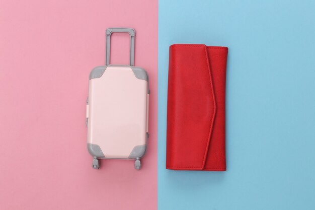 Travel concept. Mini plastic travel suitcase and purse on pink blue pastel background. Minimal style. Top view, flat lay